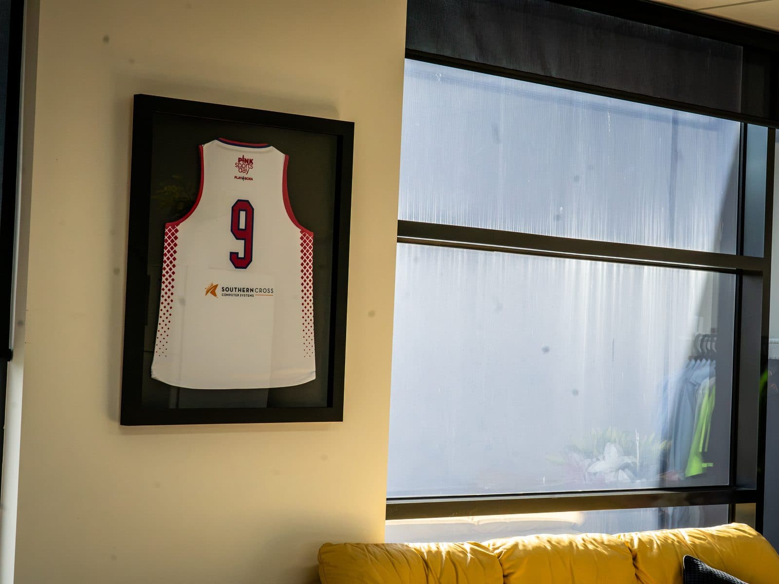 A framed Play4BCNA Pink Sports Day jersey on the wall of the SCCS office